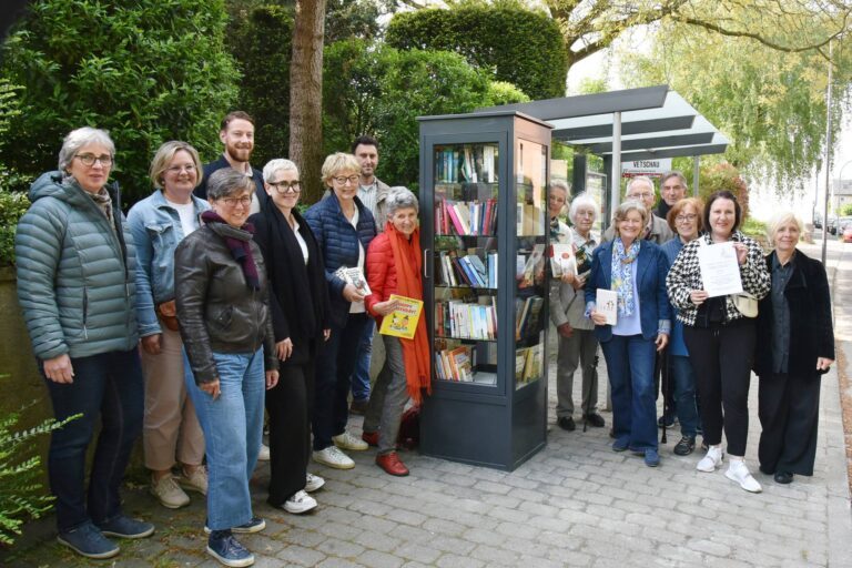 Bezirksamtsleiterin von Aachen-Richterich, Yvonne Moritz, Bezirksamtsleiterin von Aachen-Laurensberg, Lara Roosen, (erste Reihe, v. l.) und Bezirksbürgermeisterin von Aachen-Laurensberg, Petra Perschon-Adamy (erste Reihe, Vierte v. r.), feierten mit vielen Mitwirkenden die Eröffnung des bereits gut gefüllten Bücherschranks. Copyright © Stadt Aachen / Andreas Herrmann