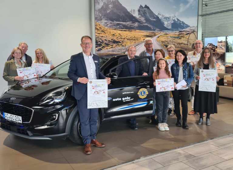 Menschen vor einem Auto bei der Präsentation des Weihnachtskalenders 2024 vom Lions Club Alsdorf